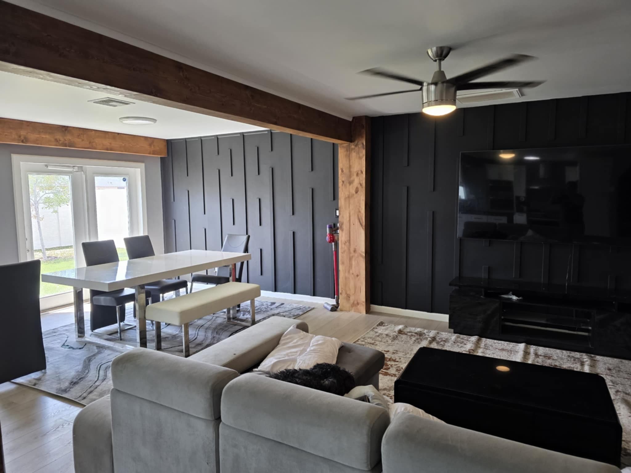 Finished open living area with wood beams, a black paneled media wall and light hardwood flooring